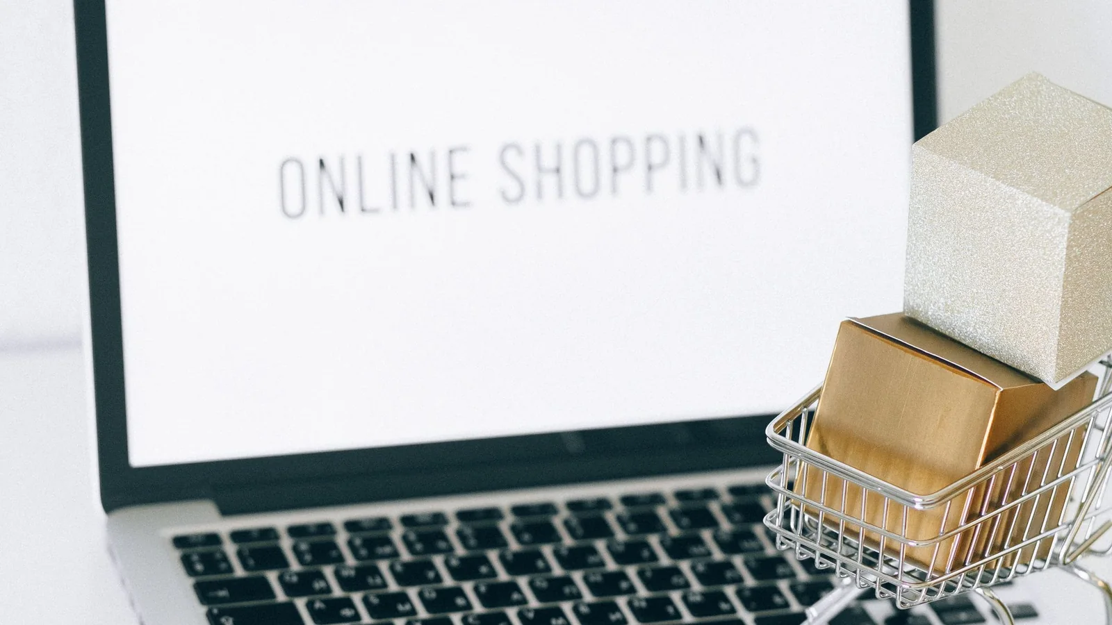Ekranında online shopping yazan dizüstü bilgisayar ve hediye kutulu mini alışveriş arabası